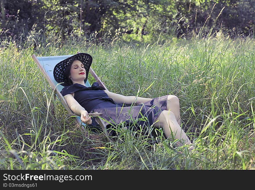 Beautiful woman relaxing on a deckchair on a green meadow