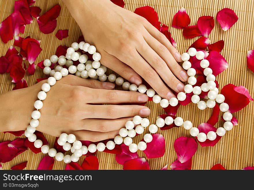 Close-up of beautiful hand braided with pearls and lie on red rose petals. Close-up of beautiful hand braided with pearls and lie on red rose petals