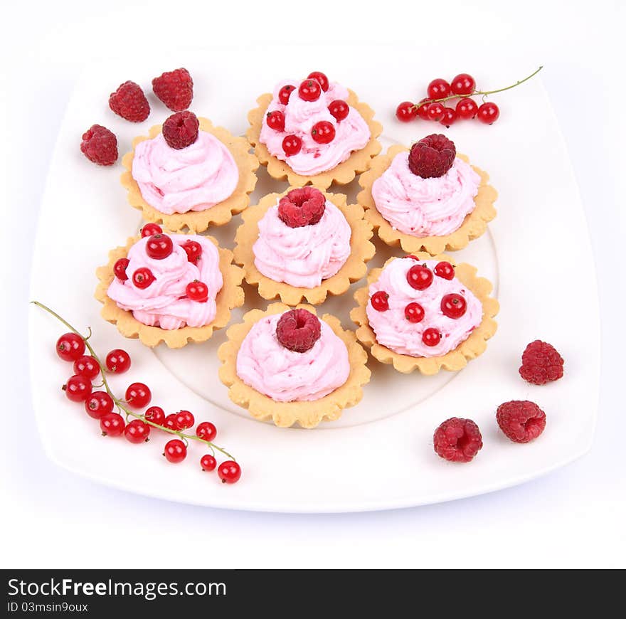 Tartlets with whipped cream, fruits and sprinkles - raspberries and redcurrants - on a plate