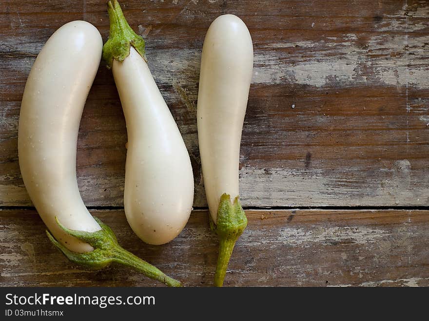 Three white mini eggplants resting on an old wooden table. Three white mini eggplants resting on an old wooden table.