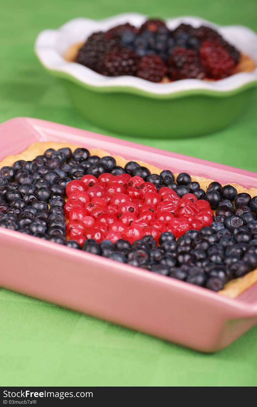 Tart with redcurrants and blueberries in a pink pottery cake tin. A tart with blueberries and raspberries out of focus in the background. Selective focus, shallow DOF. Tart with redcurrants and blueberries in a pink pottery cake tin. A tart with blueberries and raspberries out of focus in the background. Selective focus, shallow DOF.