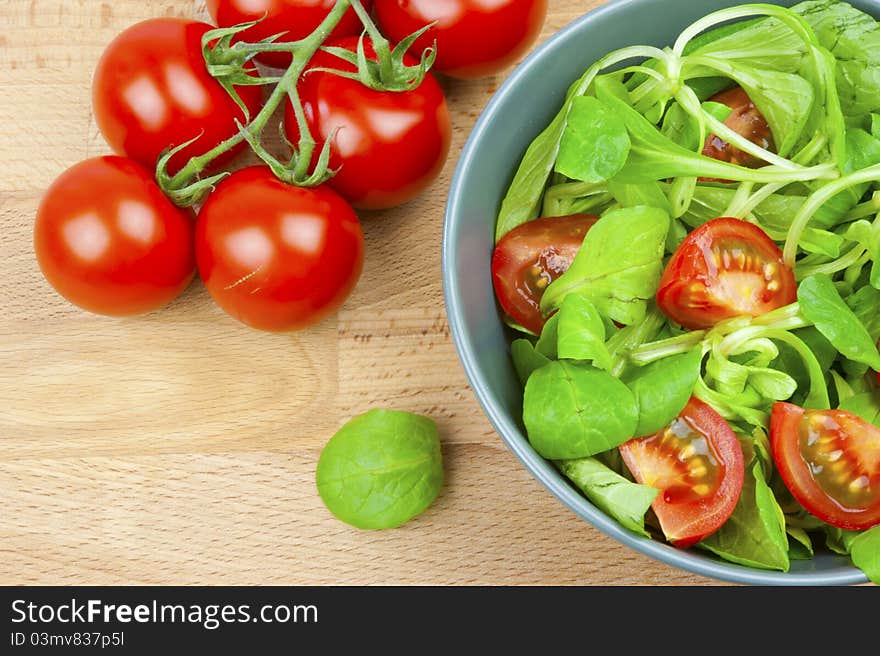 Fresh lettuce and tomatoes in a bowl, a branch of a tomato on a wooden table. Fresh lettuce and tomatoes in a bowl, a branch of a tomato on a wooden table