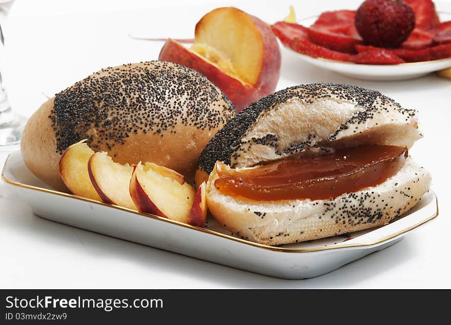 A roll with a poppy and peach jam, peach pieces and plate with the cut strawberry on a light background. A roll with a poppy and peach jam, peach pieces and plate with the cut strawberry on a light background