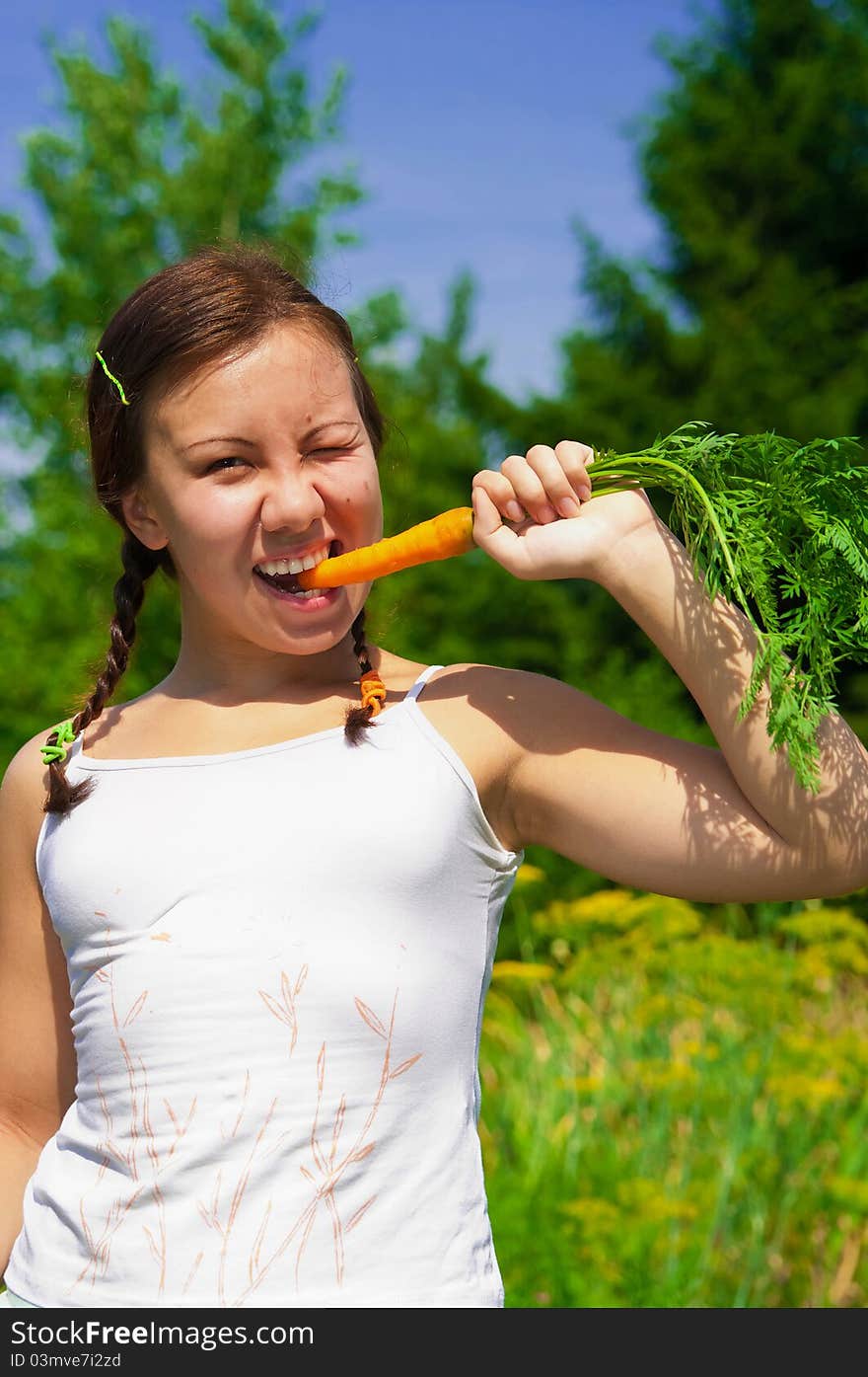 Young smiling woman bites wth effort fresh orange organic carrot in garden. Young smiling woman bites wth effort fresh orange organic carrot in garden