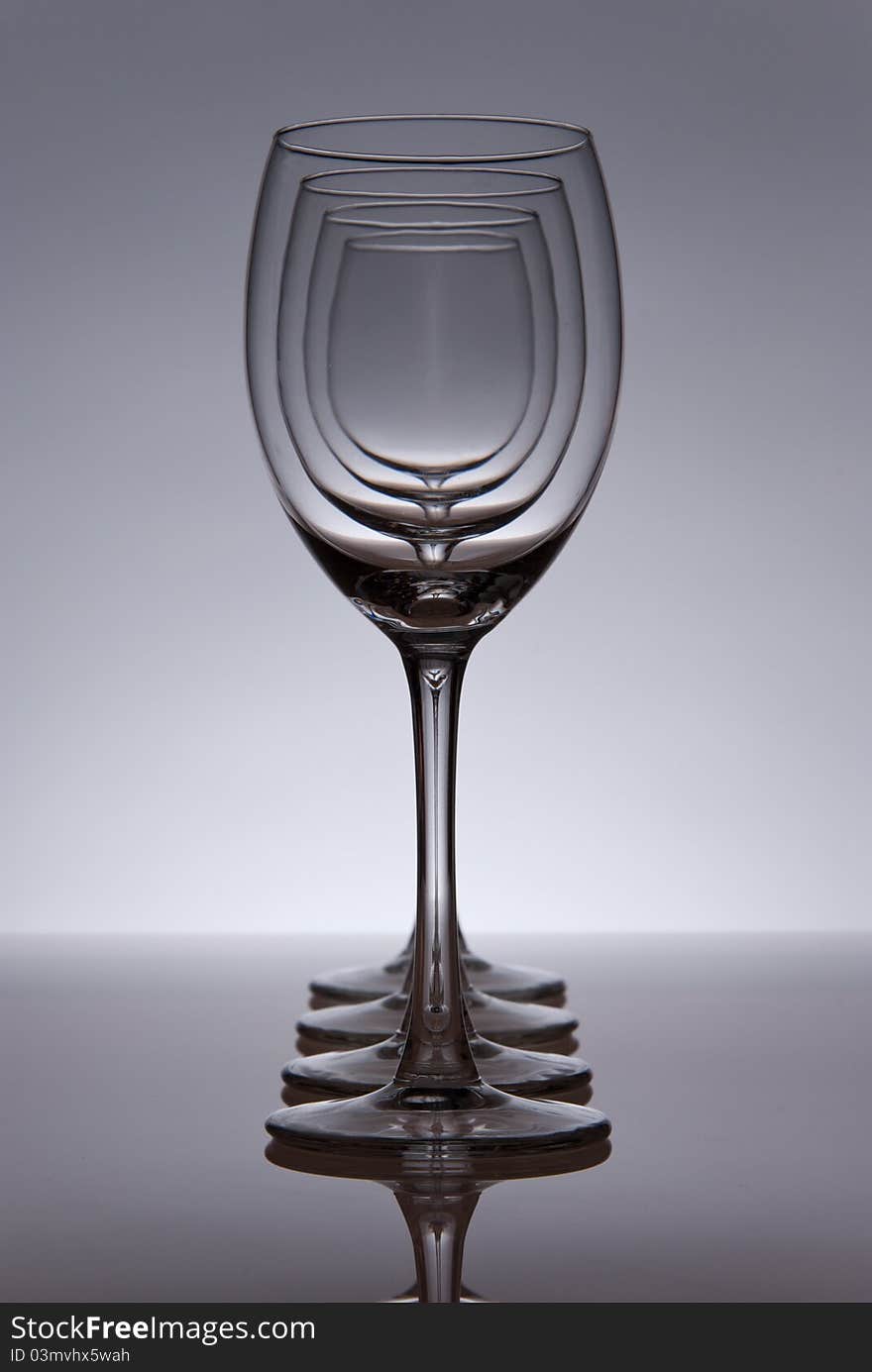 Four empty wine glasses in line. Grey table and background. Light from behind.