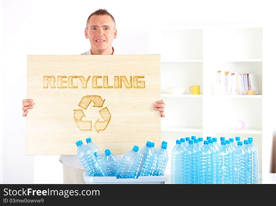 Happy man holding wooden board with word recycling and bin full of plastic blue bottles. Happy man holding wooden board with word recycling and bin full of plastic blue bottles