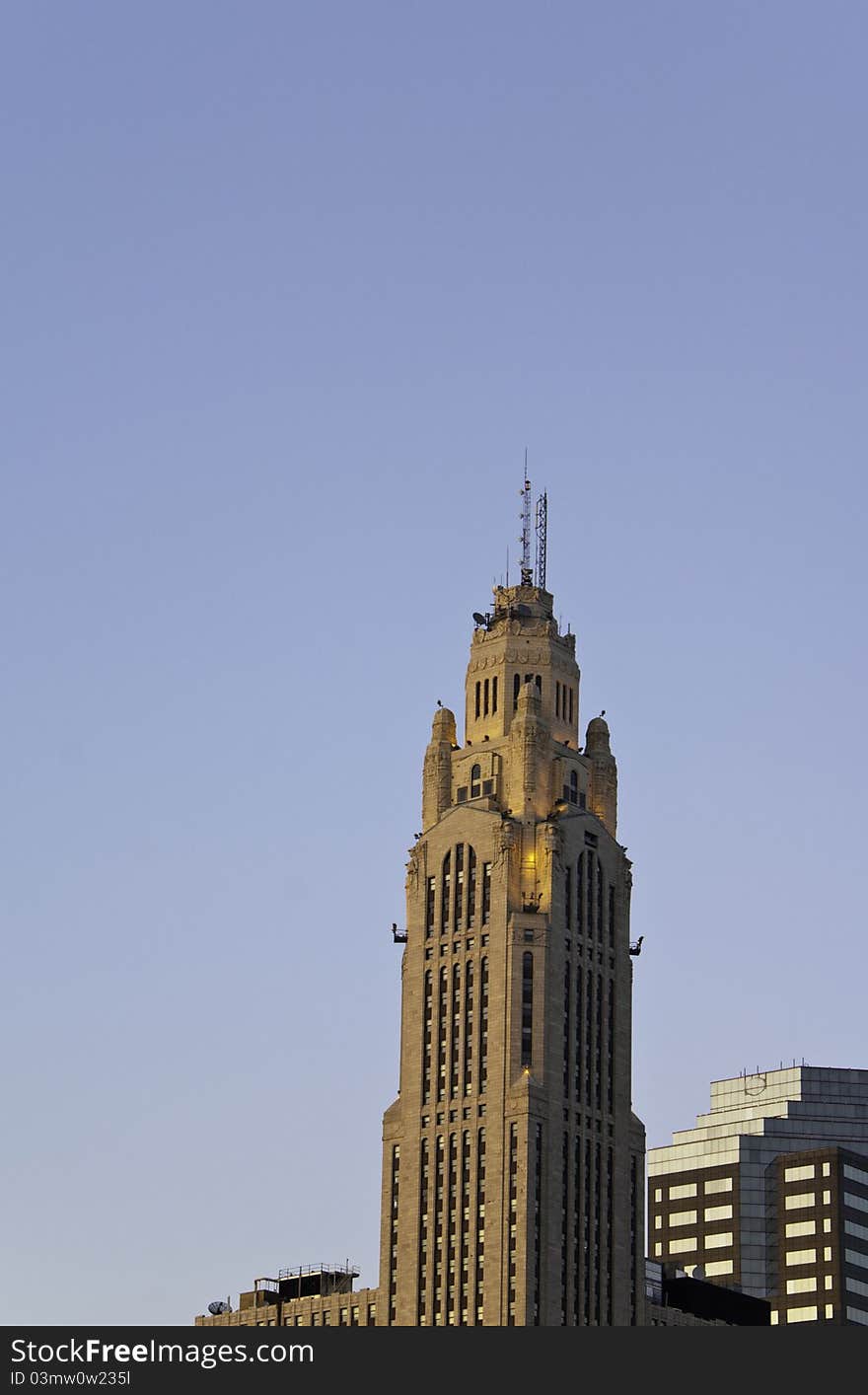 A skyscrapper reaching into the sky with smaller buildings around.