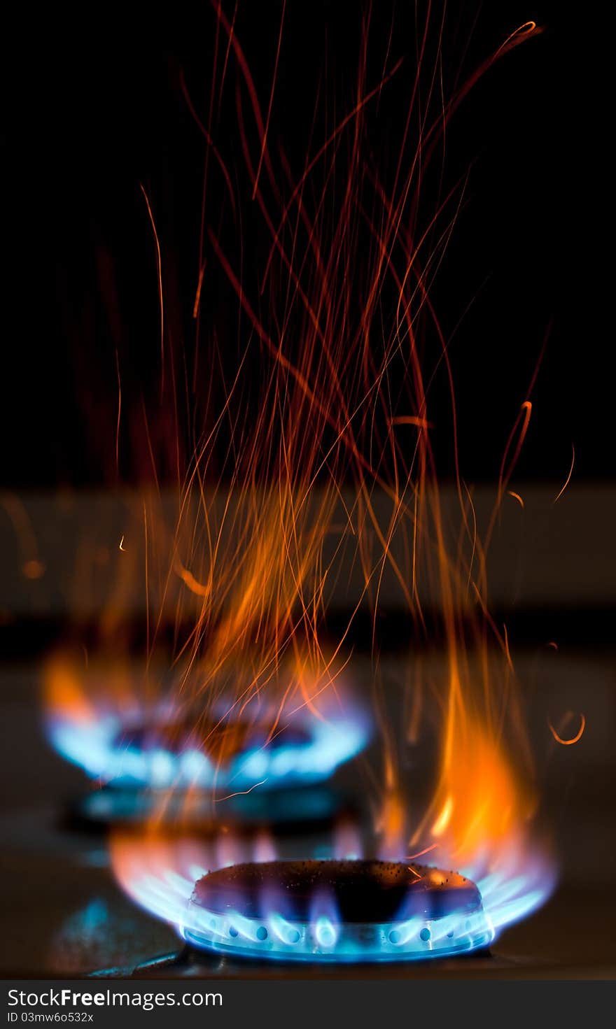 Sparks and flames above gas stove burning with blue flames