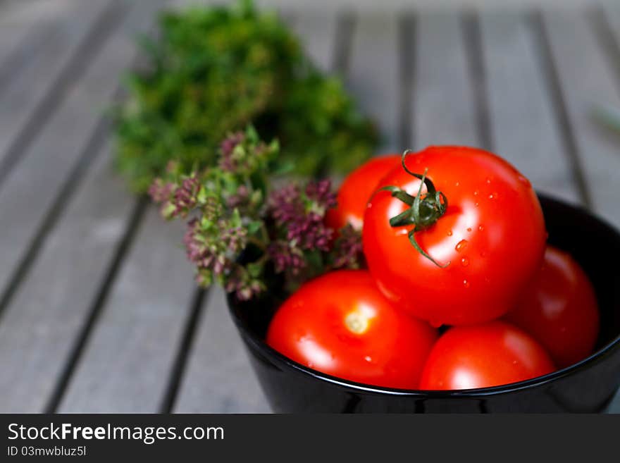 Red tTomatoes in black bowl with herbs