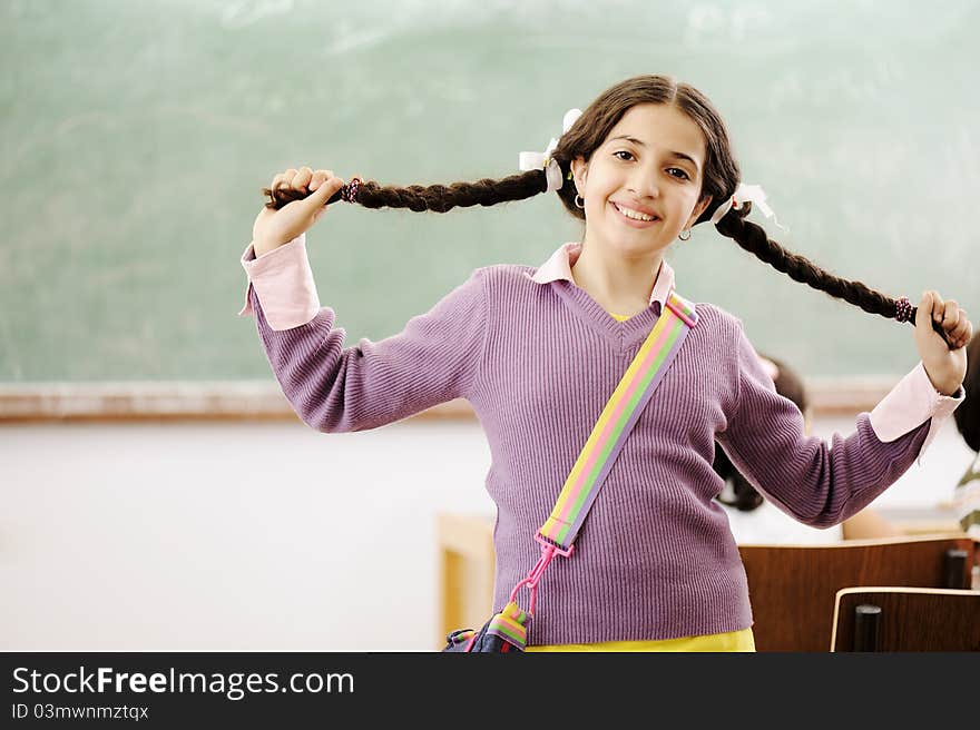 Gorgeous girl holding her hair and standing in classroom in front of board