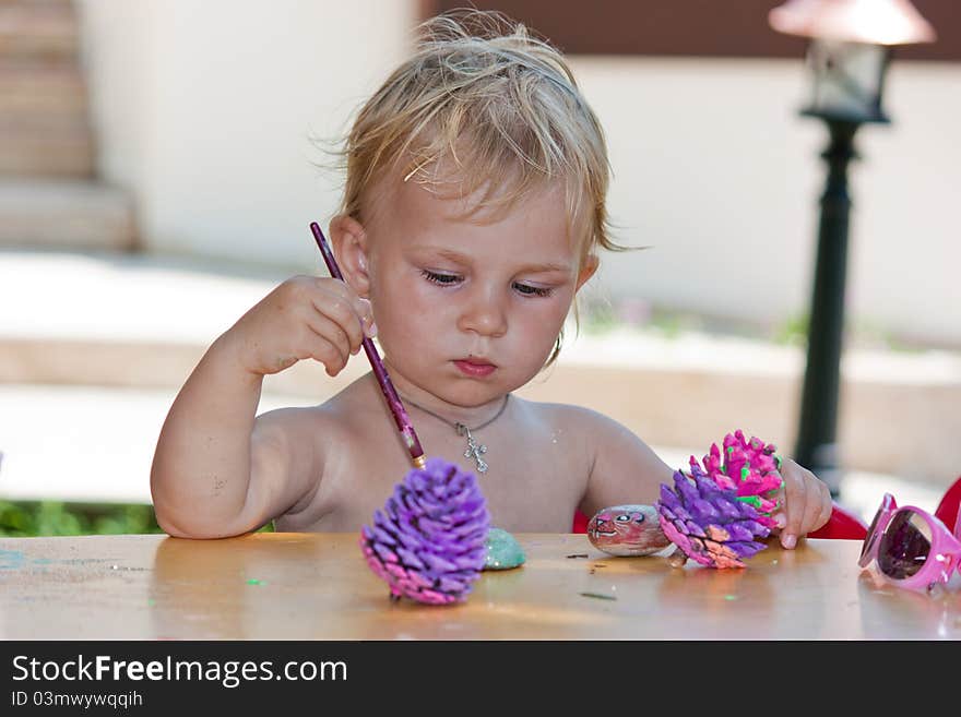 Beautiful baby girl painting beach pebbles and pine cones outdoor