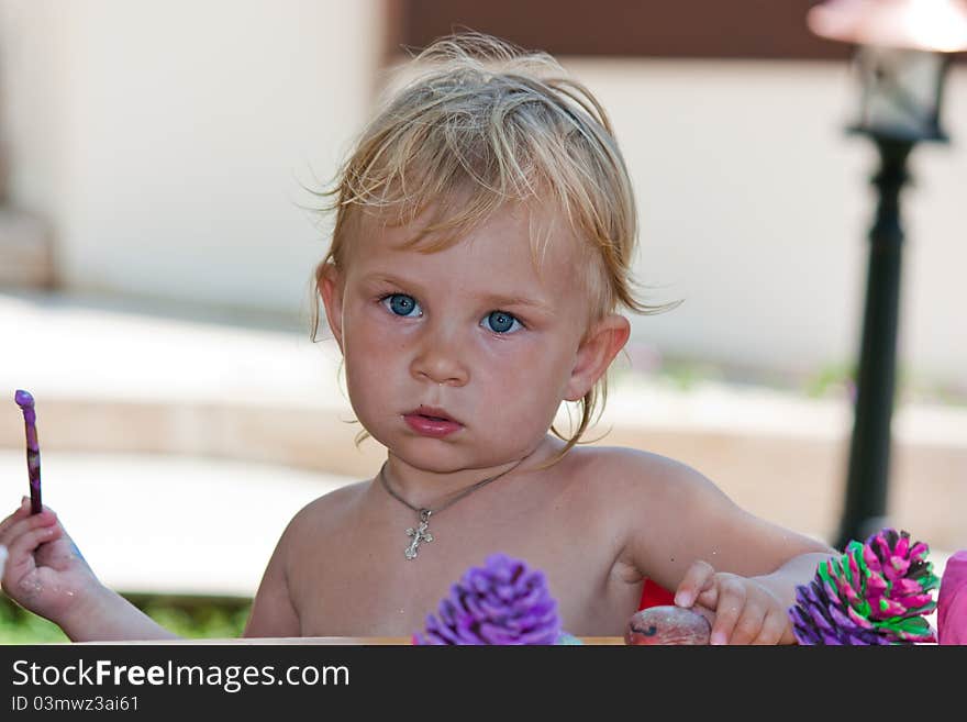 Beautiful baby girl painting beach pebbles and pine cones outdoor