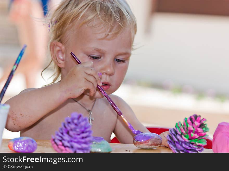 Beautiful baby girl painting beach pebbles and pine cones outdoor