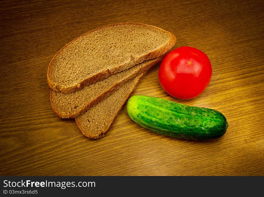 Bread, tomato and cucumber on a wooden background