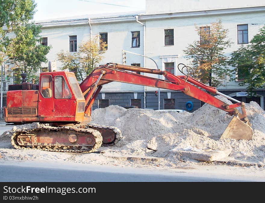 Red excavator with tracks at road repairing works