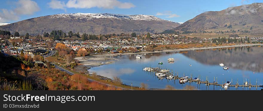 Panoramic view of popular tourist destination Wanaka Township on the shores of beautiful Lake Wanaka, Otago, New Zealand. In the foreground is the Wanaka jetty and cruise boats. Panoramic view of popular tourist destination Wanaka Township on the shores of beautiful Lake Wanaka, Otago, New Zealand. In the foreground is the Wanaka jetty and cruise boats.