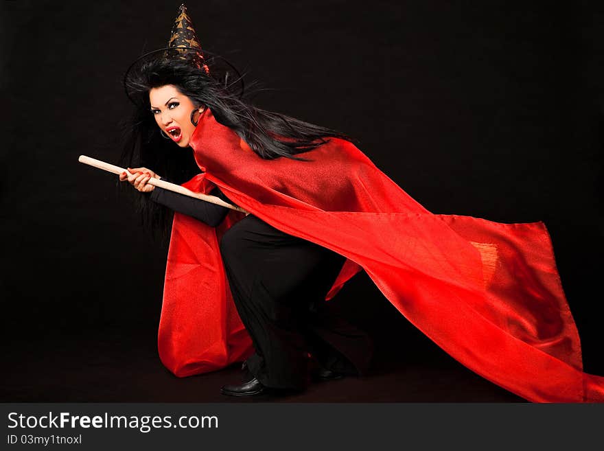 Female in witch costume with red cloak and broom between her legs screaming. Female in witch costume with red cloak and broom between her legs screaming