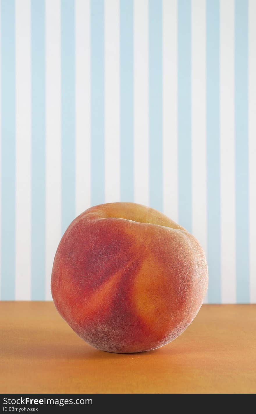 One peach on an orange table against an old-fashioned blue-white striped wallpaper. One peach on an orange table against an old-fashioned blue-white striped wallpaper.