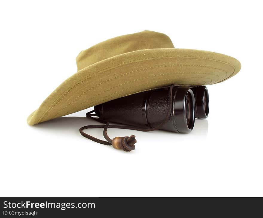 Old hikers hat with a pair of black binoculars on a white background. Old hikers hat with a pair of black binoculars on a white background