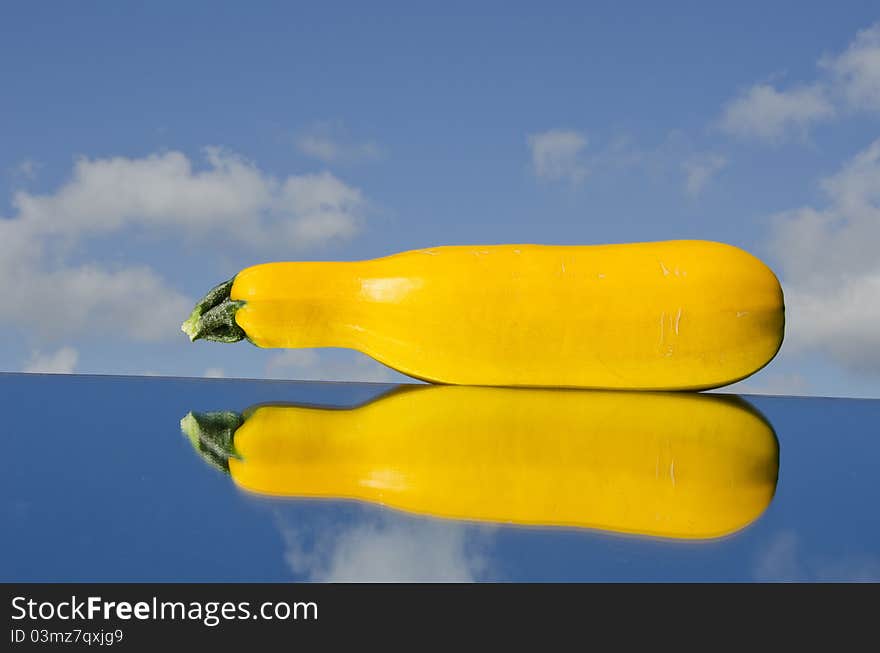 Yellow courgette on mirror and sky