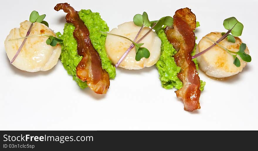 Pan-fried scallops with pea puree and bacon slices garnished with micro herbs. Pan-fried scallops with pea puree and bacon slices garnished with micro herbs