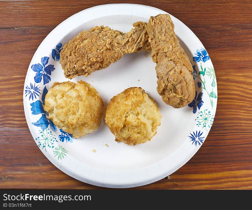 Fried chicken and biscuits on a paper plate and wood table.