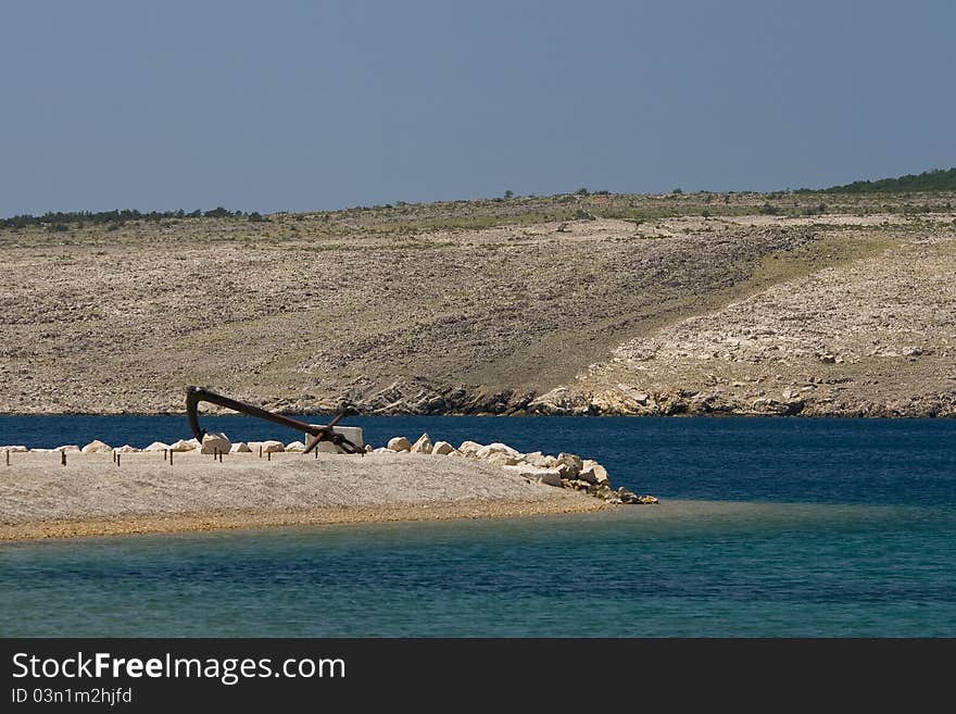 Reef with an old anchor with the barren land of the island