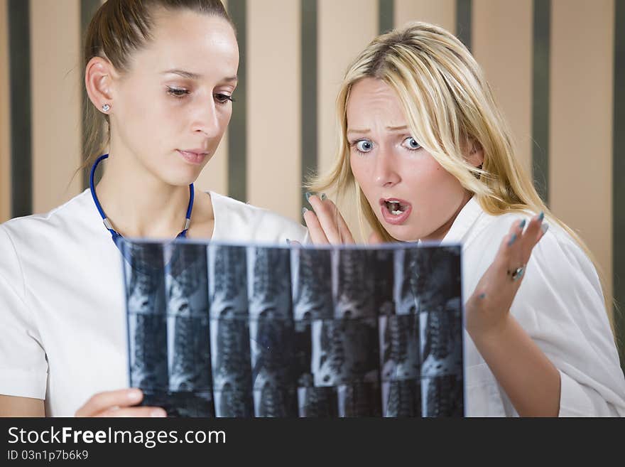 Two women doctors reading radiology scans of patient spine - shocked diagnosis scene. Two women doctors reading radiology scans of patient spine - shocked diagnosis scene.