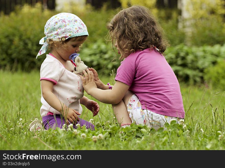 Two small girls, sisters are sitting, playing in the garden. Two small girls, sisters are sitting, playing in the garden