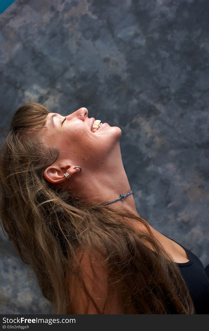 A profile portrait of a beautiful brunette with her head tilted back as she smiles and laughs against a mottled background. A profile portrait of a beautiful brunette with her head tilted back as she smiles and laughs against a mottled background.