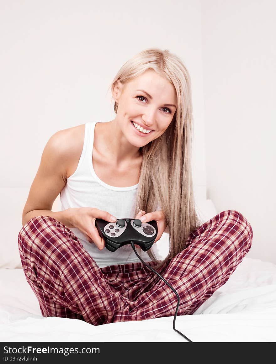 Beautiful young blond woman playing computer games on the bed at home