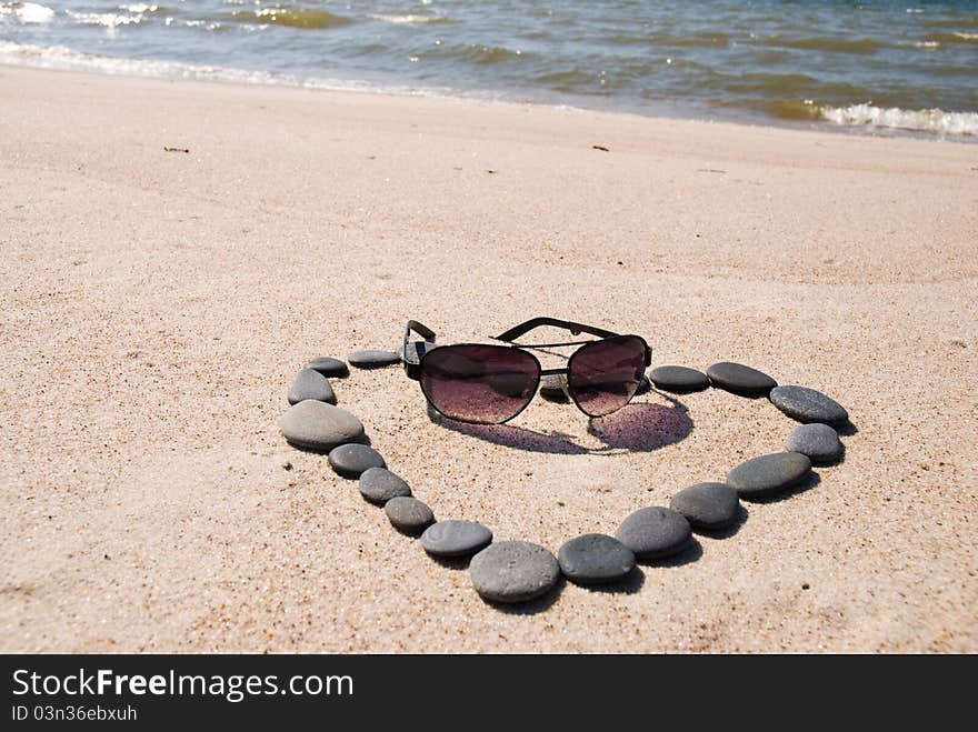 Heart from stones and sunglasses on the beach