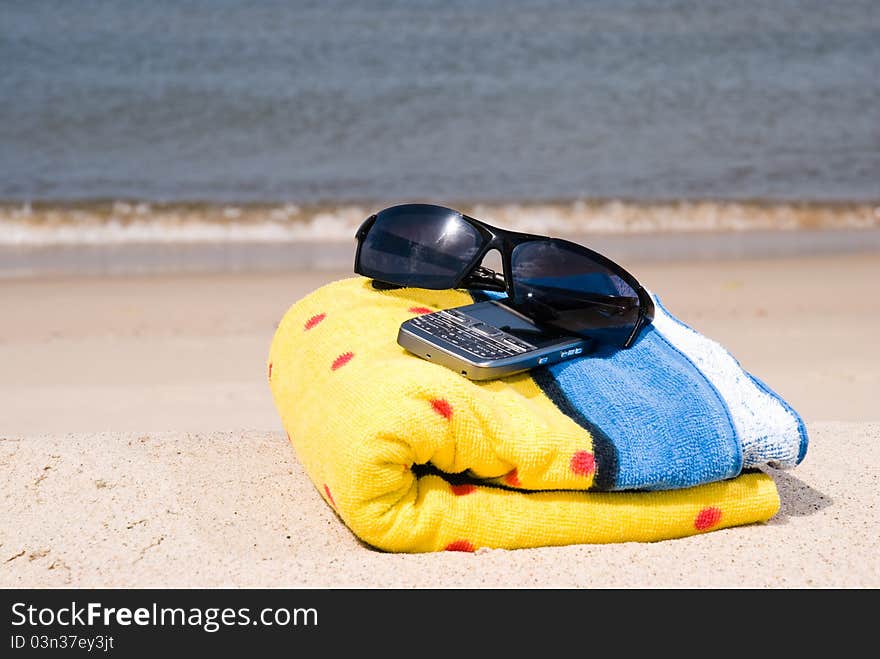 Towel, mobile phone and sunglasse on the seashore