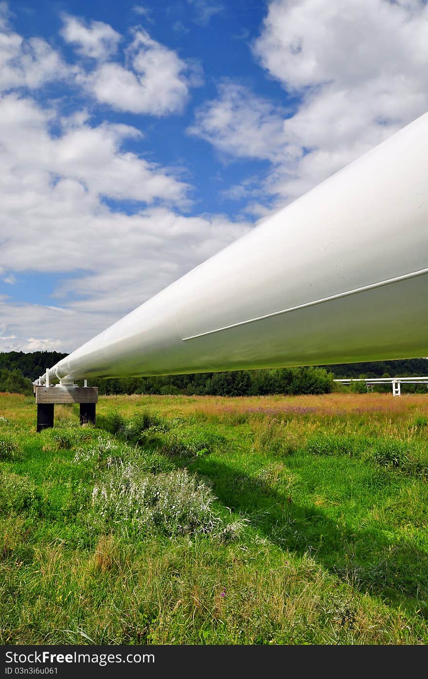 The high pressure pipeline in a summer landscape with the dark blue sky and clouds.