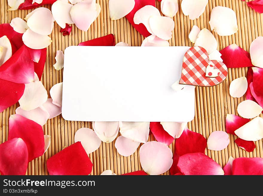 At the rose petals is white piece of paper and a red rose. Postcard. At the rose petals is white piece of paper and a red rose. Postcard