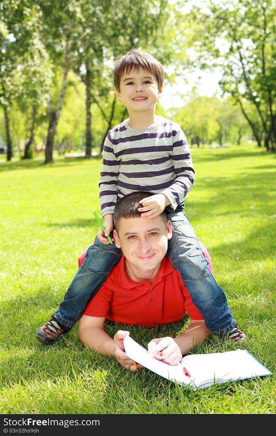 Father with his son reading together in the summer park. Father with his son reading together in the summer park