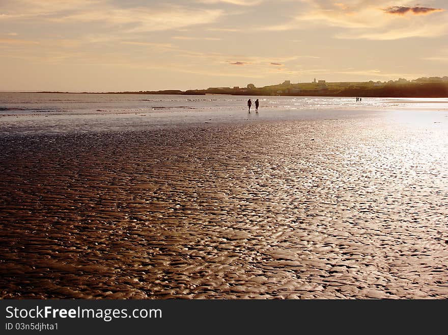 Two people walk along the shore of a quite beach at low tide. Two people walk along the shore of a quite beach at low tide