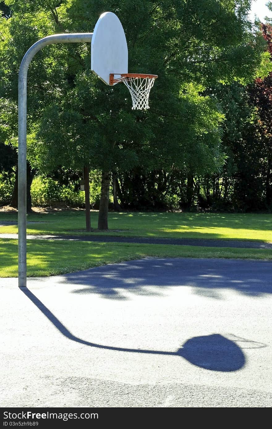 Basketball court outdoor early morning summer sun in a public park surrounded by trees. Basketball court outdoor early morning summer sun in a public park surrounded by trees.