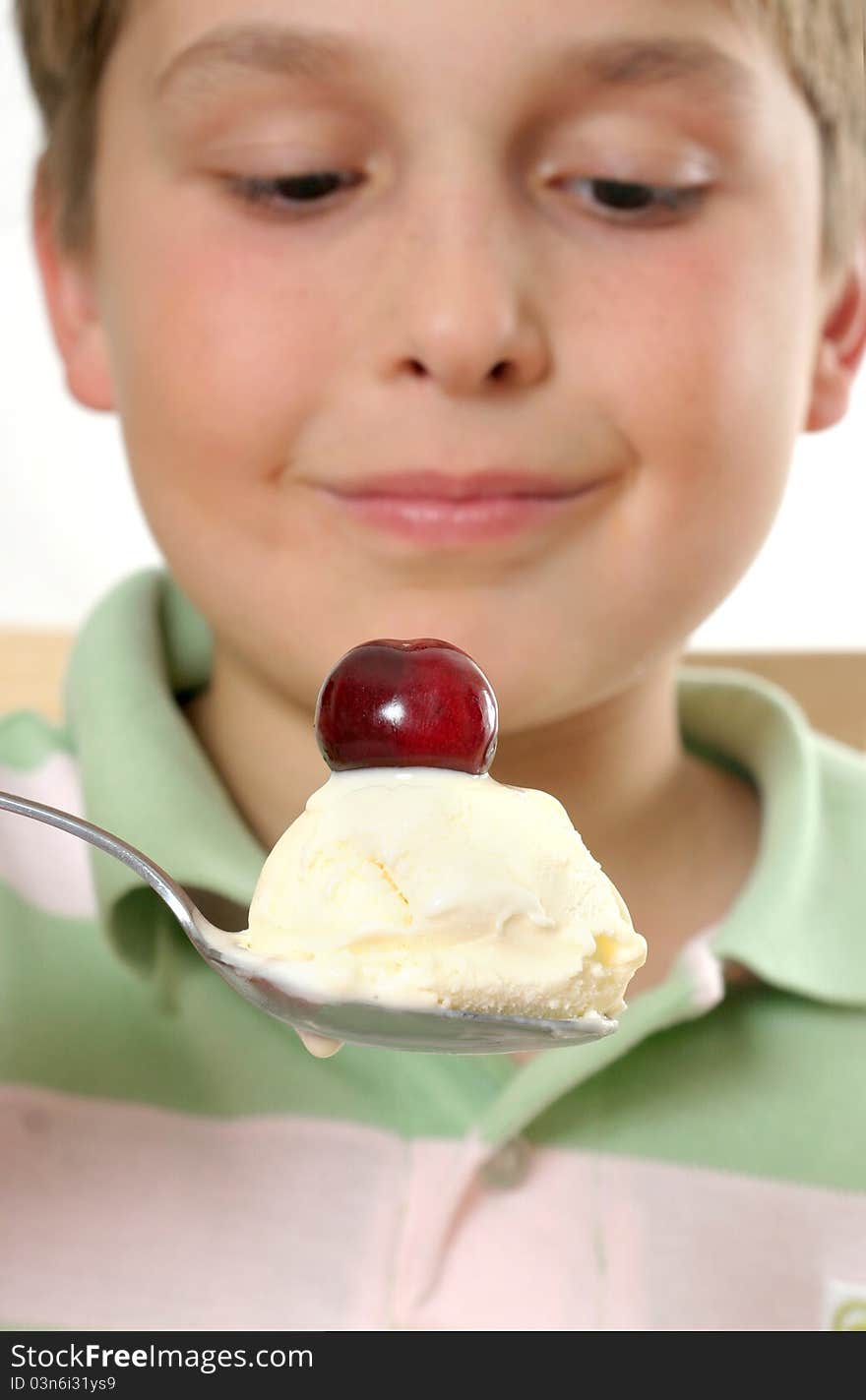 Boy scooping up and holding a spoonful of creamy ice cream with a cherry on top. Selective focus. Boy scooping up and holding a spoonful of creamy ice cream with a cherry on top. Selective focus.