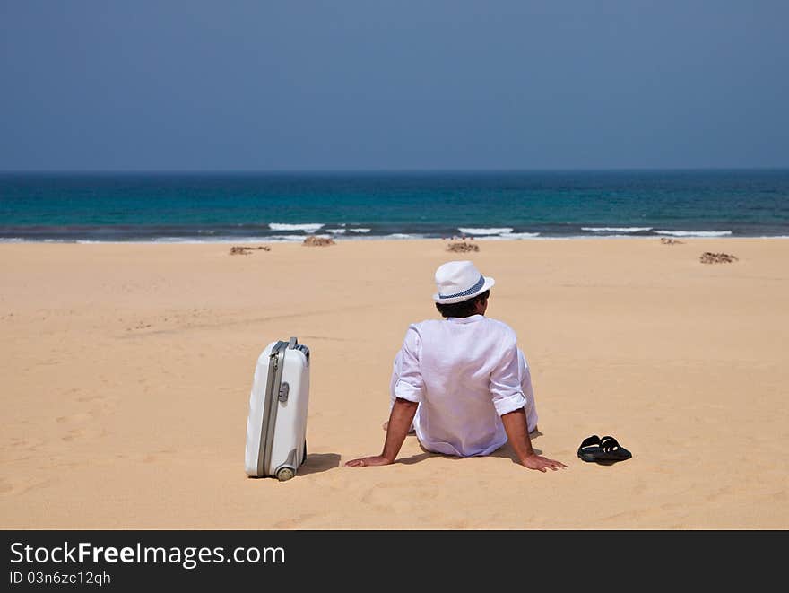 Man siting with luggage on a sand and observing sea. Man siting with luggage on a sand and observing sea