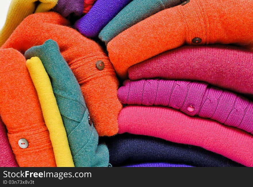 Stack of women's sweaters and cardigans in bright vivid colours against white in natural woolen fibers. Stack of women's sweaters and cardigans in bright vivid colours against white in natural woolen fibers.