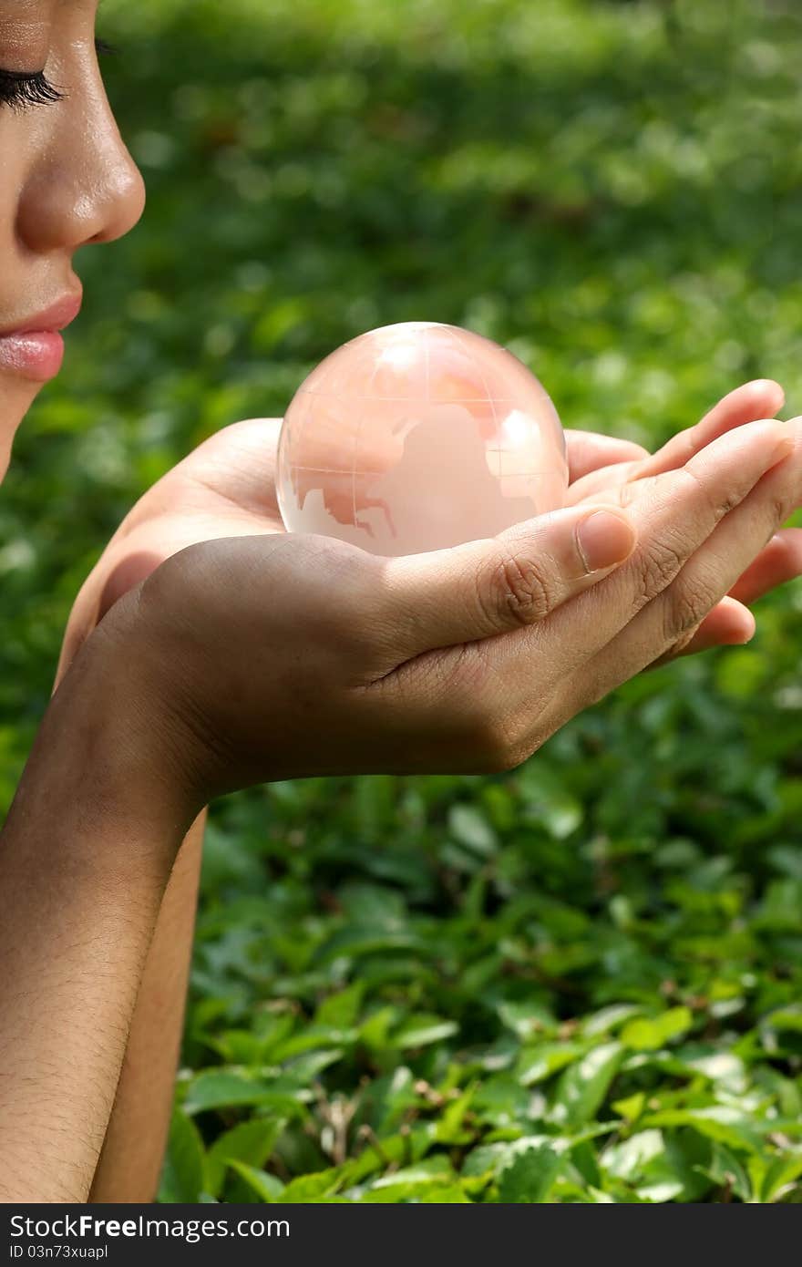 Woman face and hand with crystal globe in green leaves background