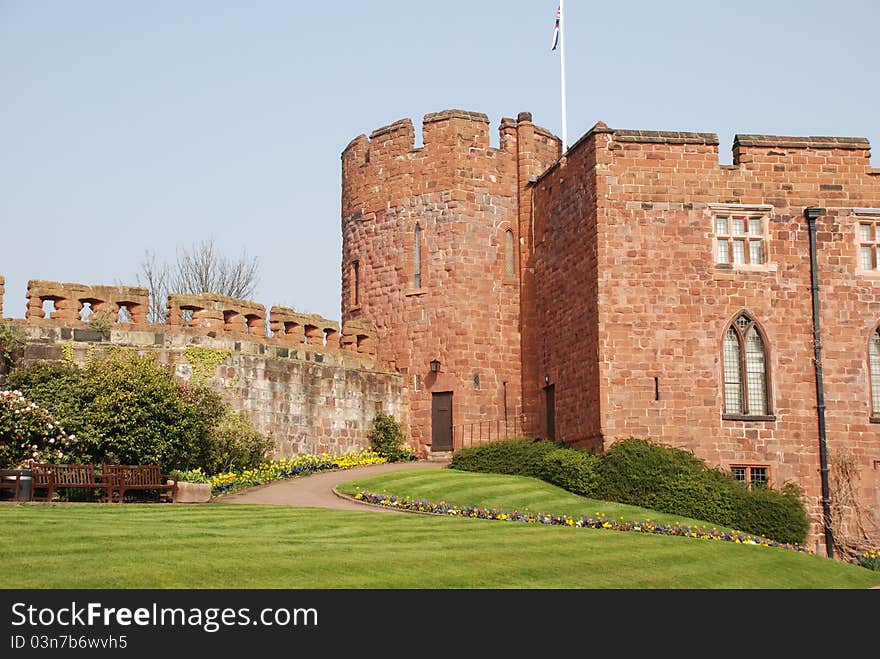 Generic castle with castellations and interesting brickwork in garden setting. Arched and mullion windows.