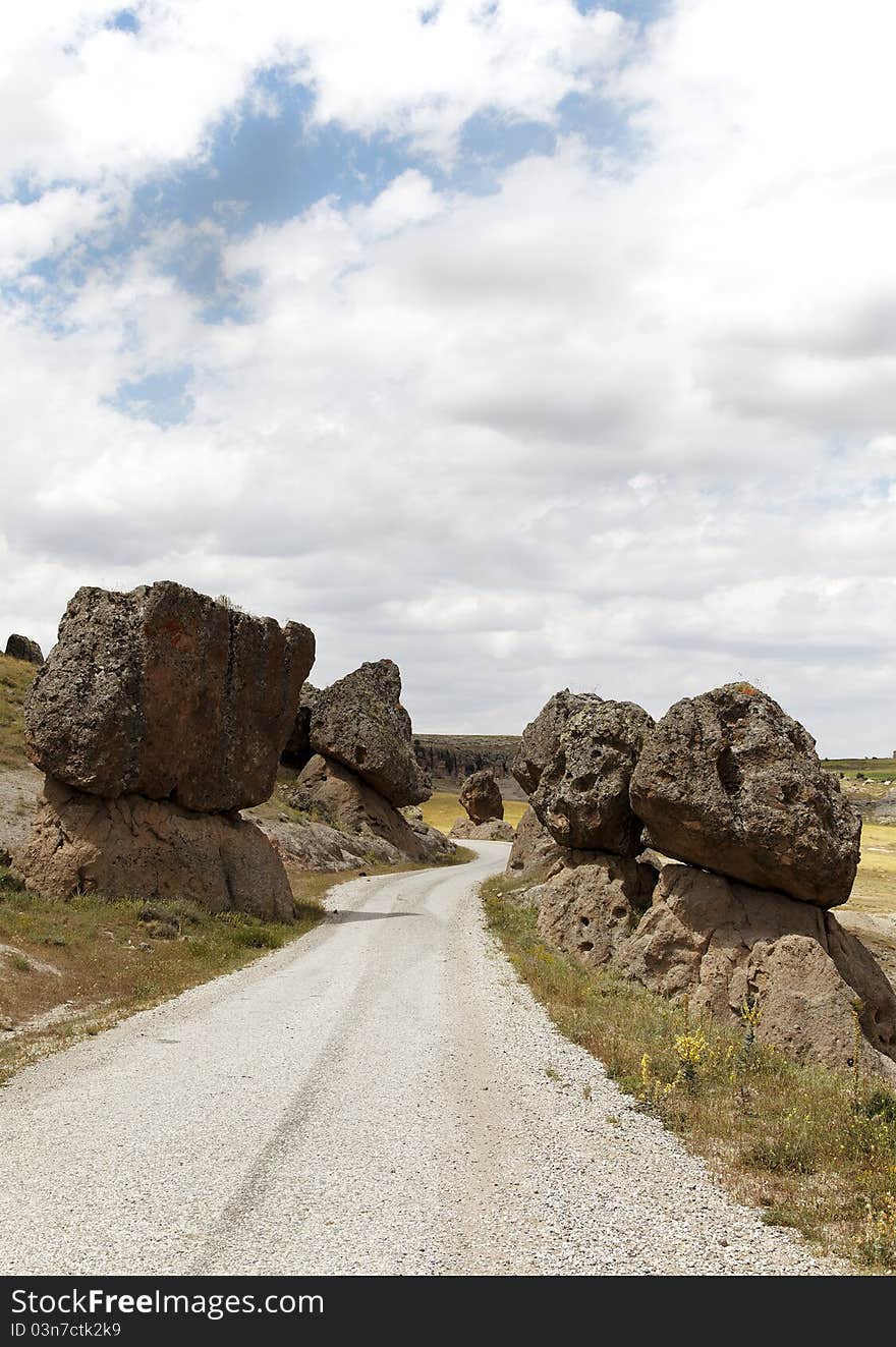 Precarious balanced volcanic rocks on either side of a public dirt track, Cappadocia, Turkey. Volcanic terrian, lava rock, limestone, sandstone, blue cloud layered sky, portrait, copy space, crop area, scenic