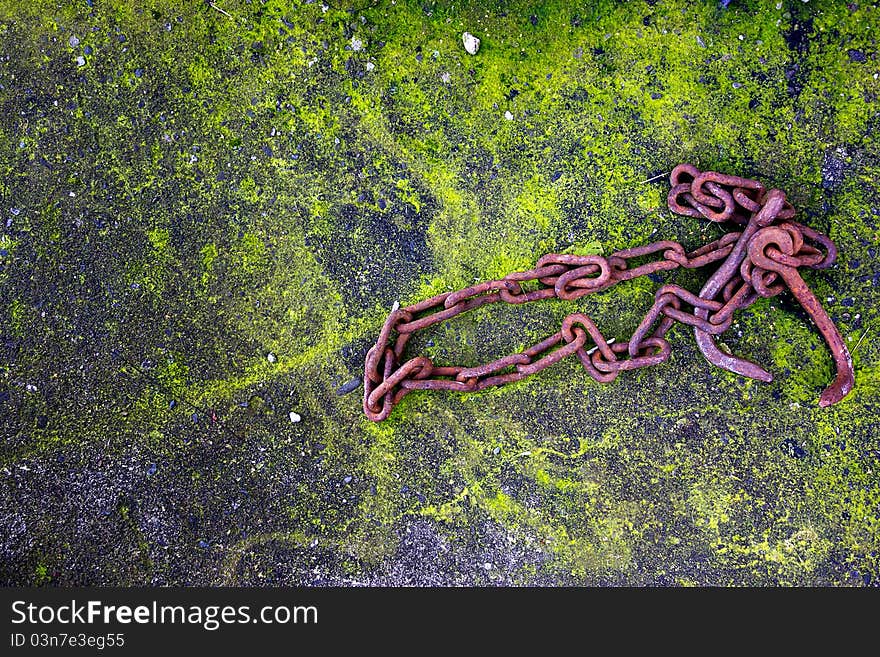 Rusty metal chain on moss-covered concrete.