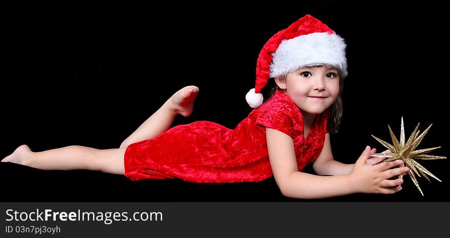 Sweet little girl in santa hat laying on floor with golden Christmas star. isolated on black. Sweet little girl in santa hat laying on floor with golden Christmas star. isolated on black