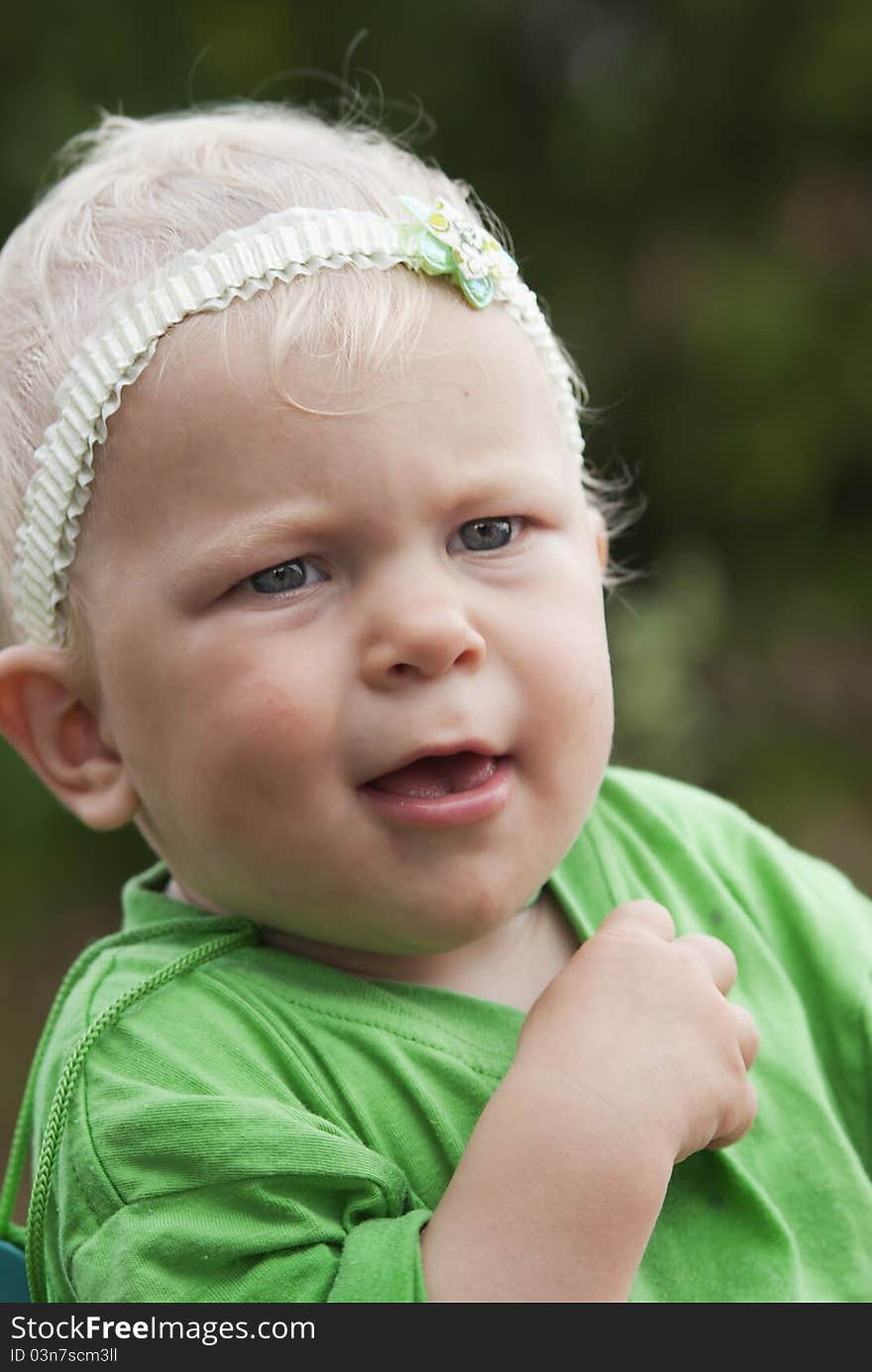 The little girl the blonde with blue eyes (11 months) in a green vest looks directly in the chamber. The little girl the blonde with blue eyes (11 months) in a green vest looks directly in the chamber