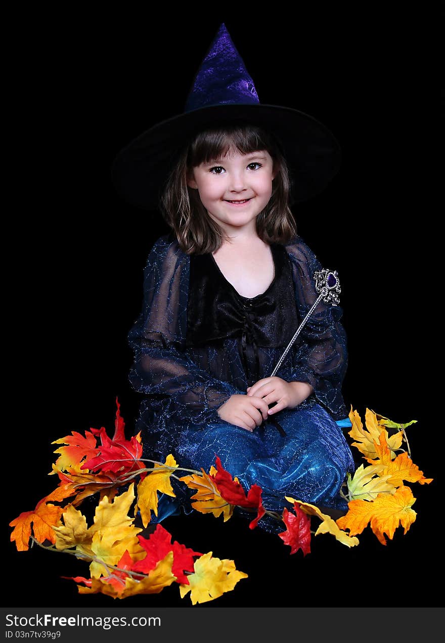 Little girl in witch costume surrounded by fall leaves and smiling. isolated on black. Little girl in witch costume surrounded by fall leaves and smiling. isolated on black