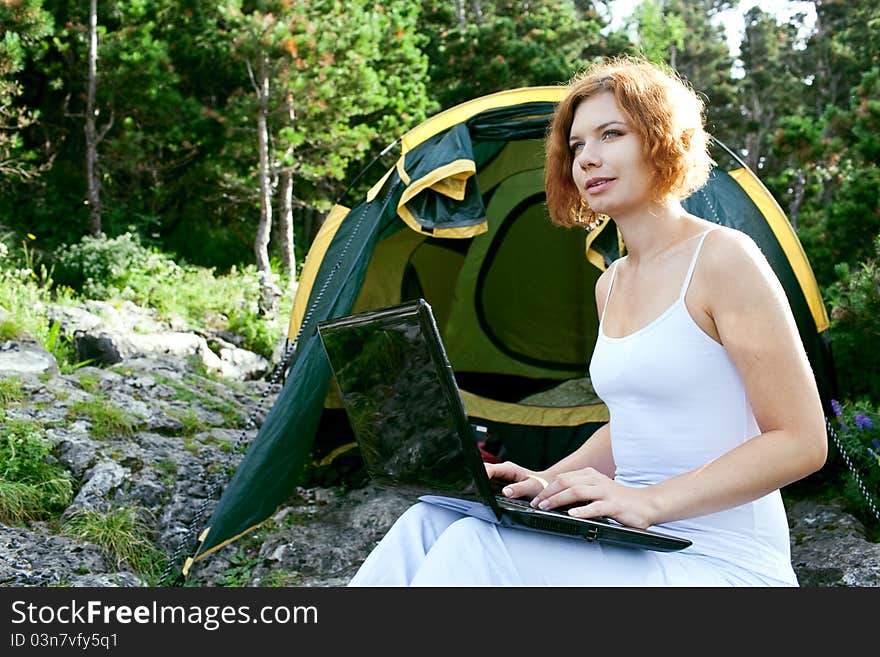 Woman sitting next to a tent with a laptop