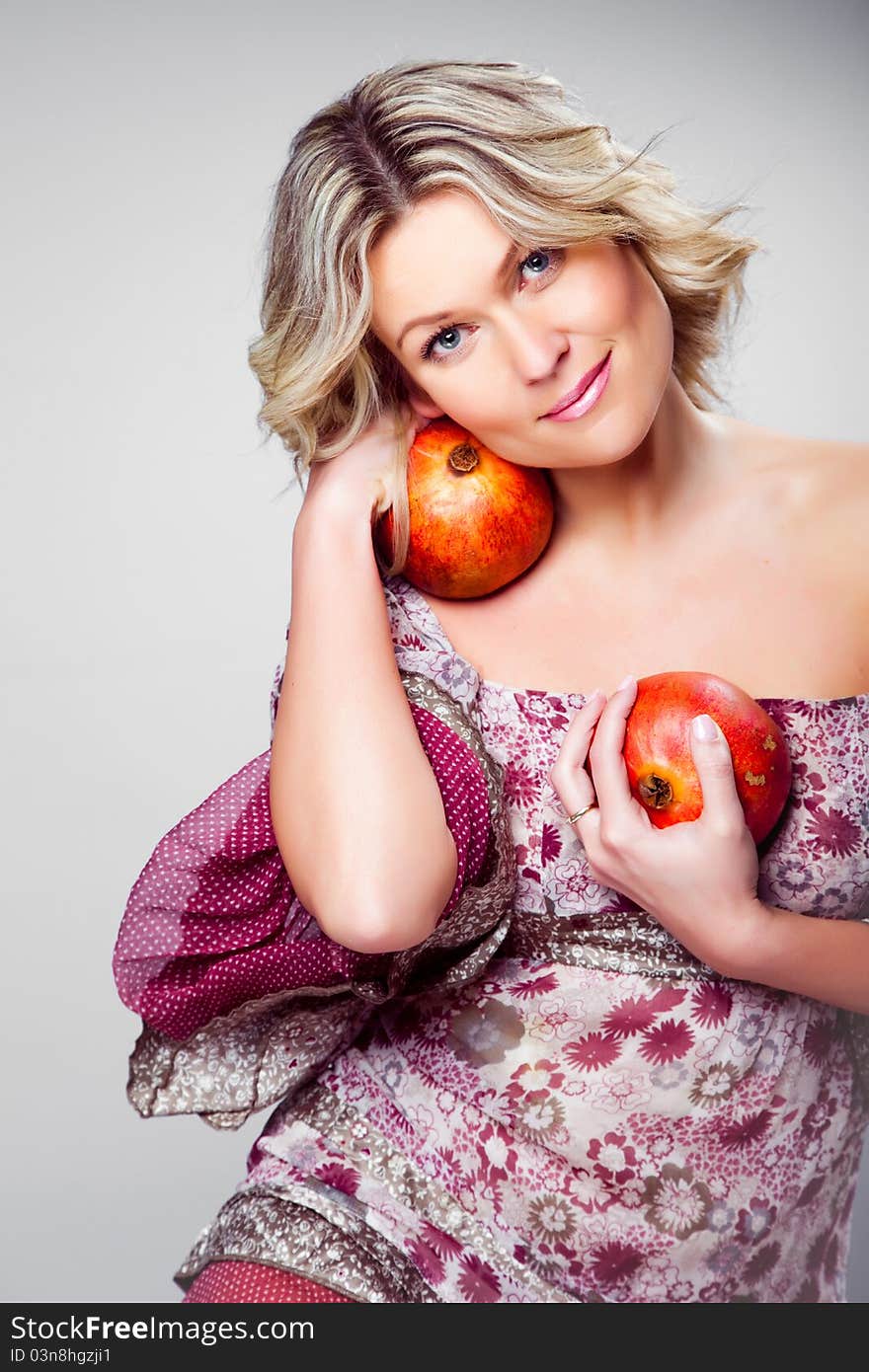 Portrait of beautiful blonde woman holding two pomegranates on grey background. Portrait of beautiful blonde woman holding two pomegranates on grey background